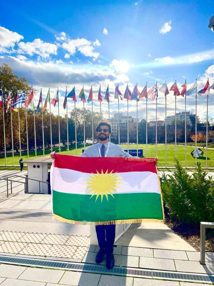 بە ئاڵای پیرۆزی كوردستان مامۆستایەكی زانكۆی سۆران بەشداری كۆڕبەندی پەرلەمانی ئەوروپا دەكات